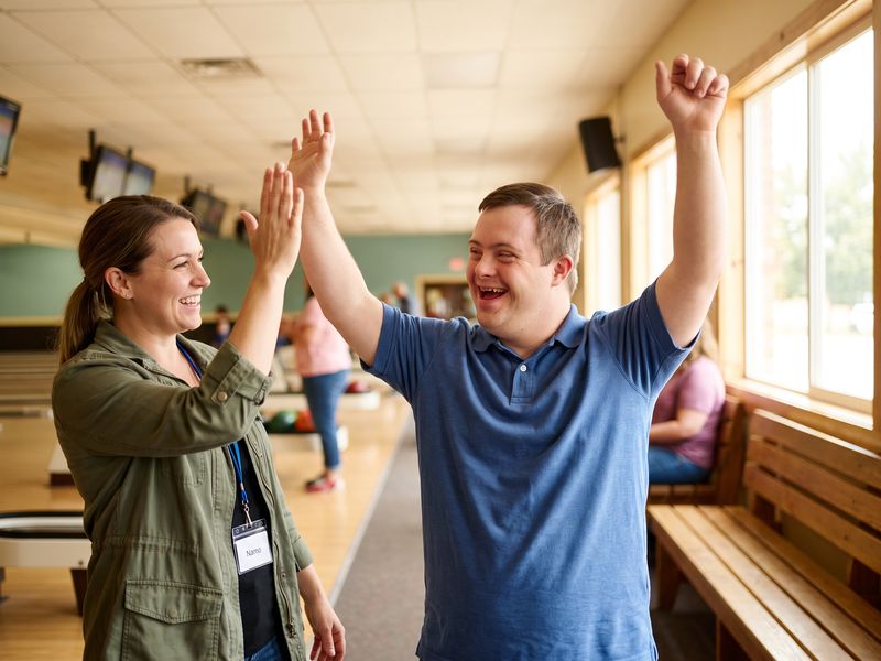 A man with Down syndrome raises his arms and high-fives his support worker after a strike at a bowling alley
